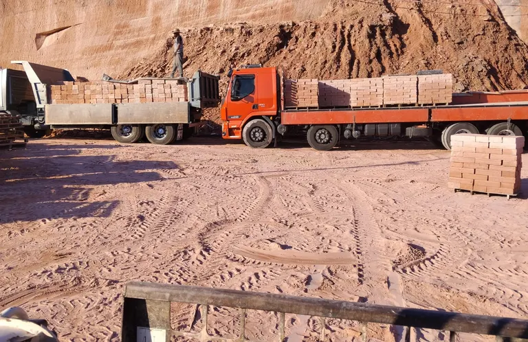 Pedras grês organizadas em cima de paletes, encima de um caminhão laranja e outro cinza, em uma pedreira em Taquara - RS